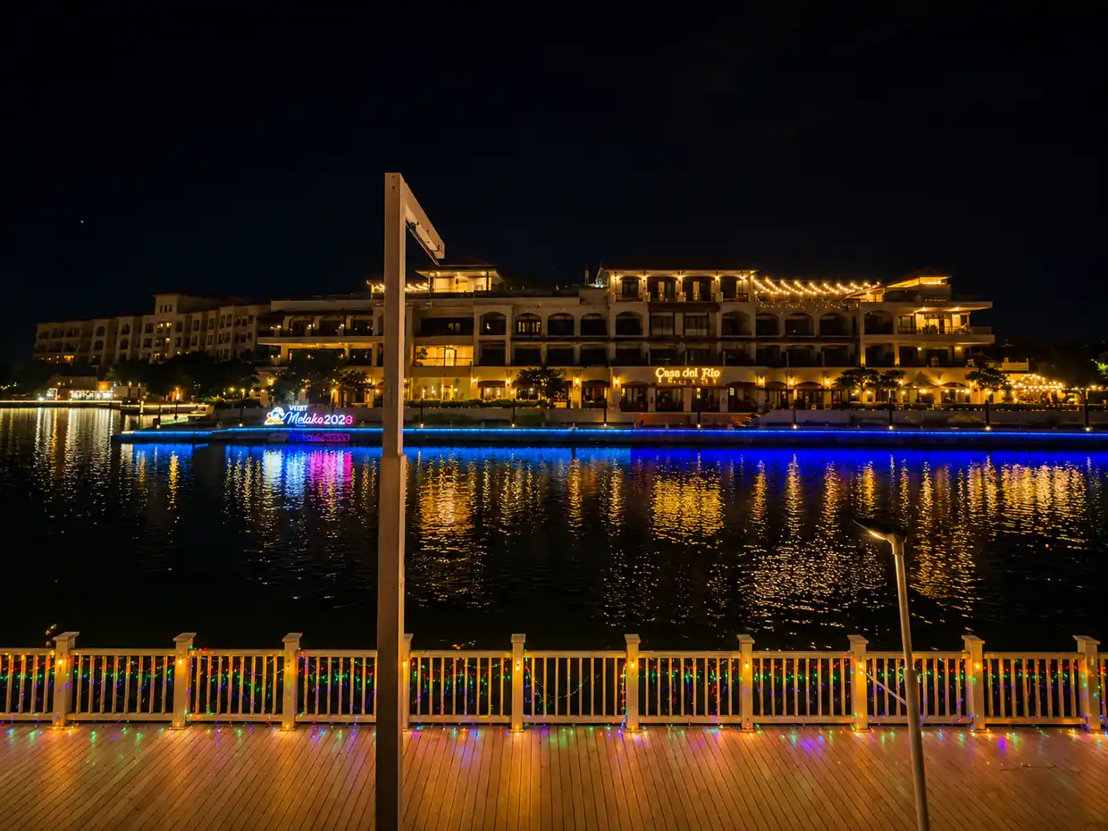 The Melaka River at night with string lights, painted shophouses and a river cruise boat on still water